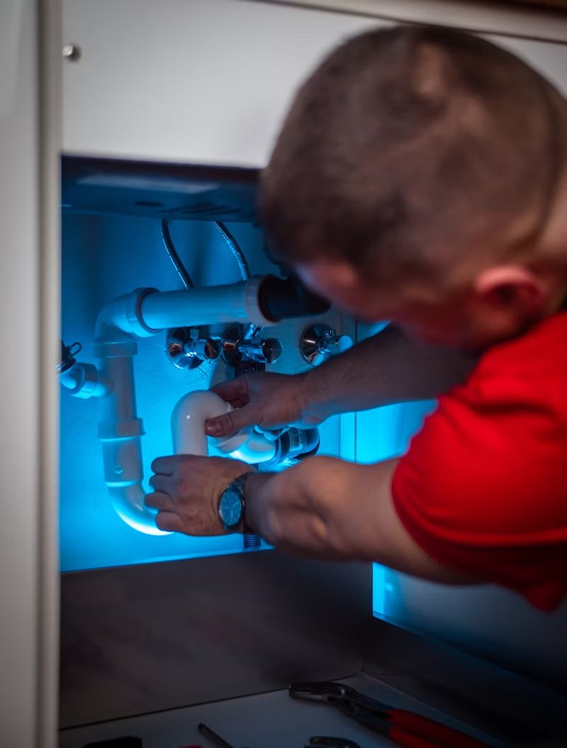 Plumber working on pipes under a cabinet