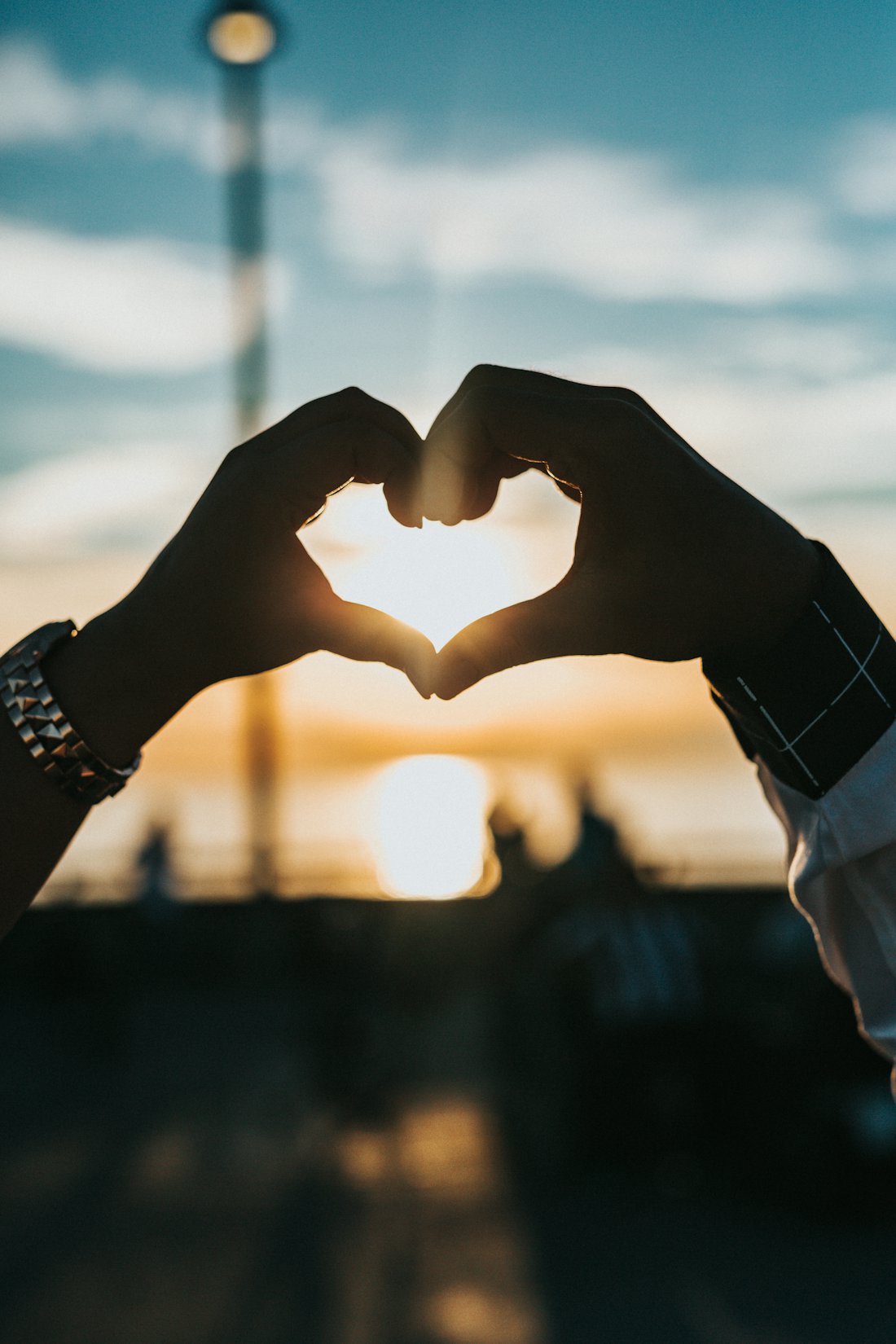 Two hands making a heart shape against the sunset