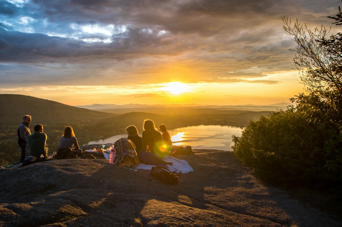 Friends sitting on a hilltop watching the sunset